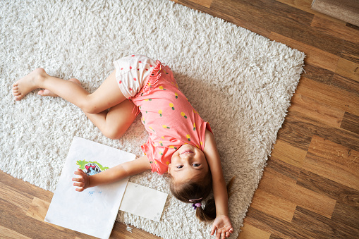 Little cute girl lying on carpet at home and smiling.