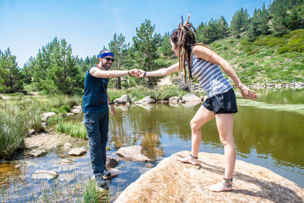 la jeune femme aide l'homme sur la roche dans un lac de montagne - vacations women men stability photos et images de collection