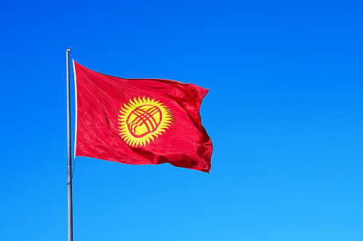 Kyrgyzstan flag on the mast on deep blue sky background. Kyrgyz republic national flag