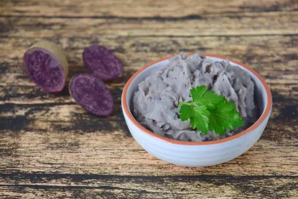 Vitelotte mashed purple potato in a bowl on wooden background garnish with parsley.