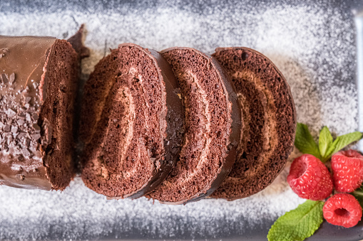 Chocolate swiss roll with jam decorated with raspberries on a plate. Sweets. Selective focus.