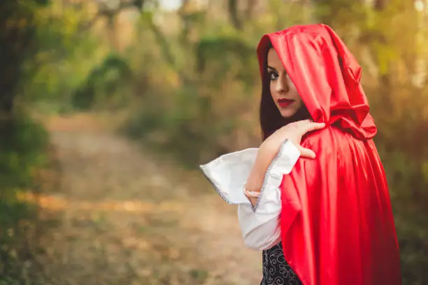 Little red riding hood looking towards sunset, seems to be lost in the forest. Waist up.