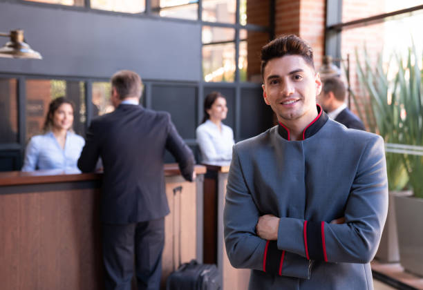 retrato de campana americana latina frente a la cámara sonriendo con los brazos cruzados y los clientes que se registran en la recepción - men latin american and hispanic ethnicity young men smiling fotografías e imágenes de stock