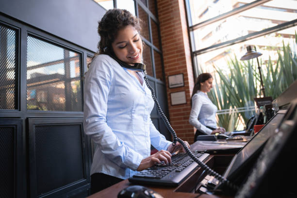 Beautiful hotel receptionist on a phone call looking at the bookings on system smiling Beautiful hotel receptionist on a phone call looking at the bookings on system smiling very happy concierge photos stock pictures, royalty-free photos & images