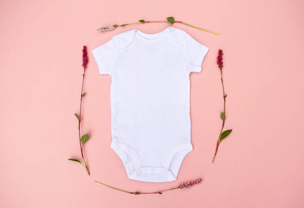 赤ちゃんピンクの背景に繊細なかわいいピンクの花に囲まれた空白の赤ちゃんの成長ボディスーツ - onesie ストックフォトと画像