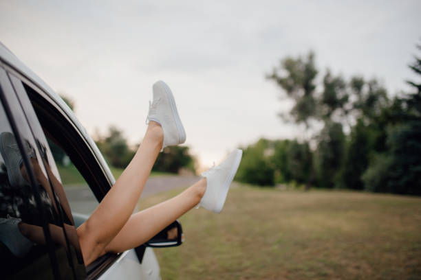istock Female legs dangling from car window with a sky on background, outdoor 1164199180