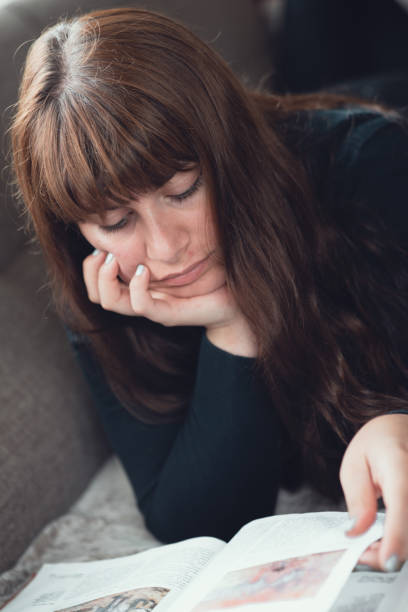 istock Portrait of woman lying down reading a book 1164200240