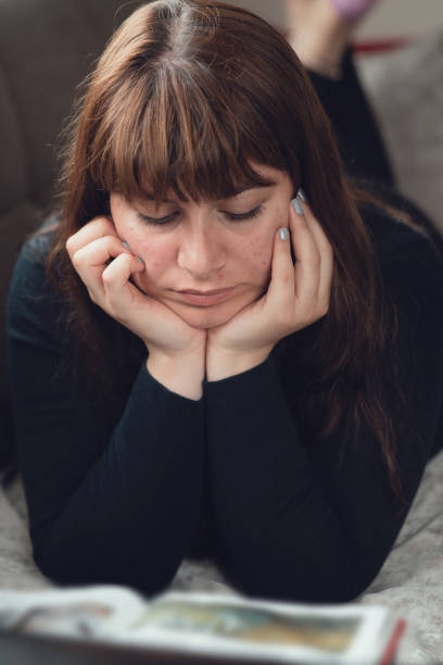istock Portrait of woman lying down reading a book 1164200632