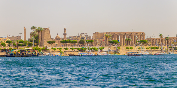 Tourists boats in the middle of the River Nile and in the background Ancient pharaonic Luxor temple in Egypt