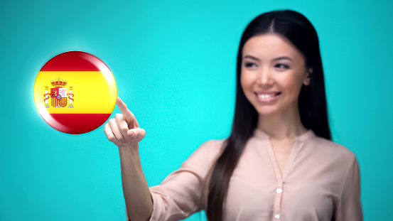 Cheerful female pushing Spanish flag button, ready to learn foreign language