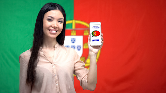 Woman holding smartphone with language study app, Portuguese flag on background