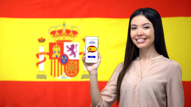 kvinnliga holding mobiltelefon med lär dig spanska app, flagga på bakgrund, utbildning - foton med speaker bildbanksfoton och bilder