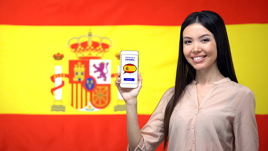 Girl holding smartphone with language study app, Spanish flag on background