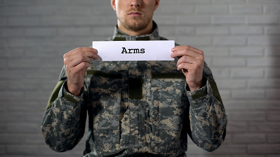 Arms word written on sign in hands of male soldier, weapon arsenal, industry