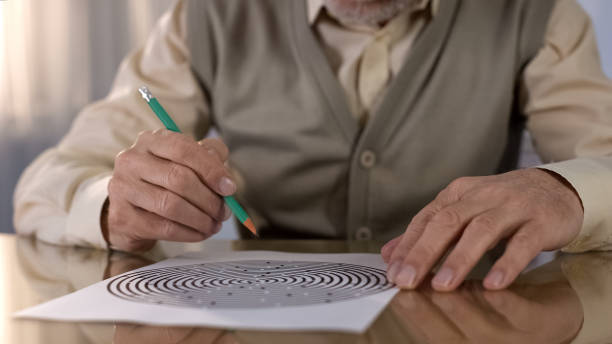 homme retraité concentré résolvant l'essai logique à la table, exercice de mémoire, neurologie - senior adult leisure games playing care photos et images de collection