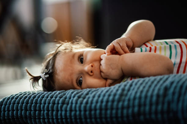 linda niña masticando sus dedos mientras está acostada en la almohada. - finger in mouth fotografías e imágenes de stock