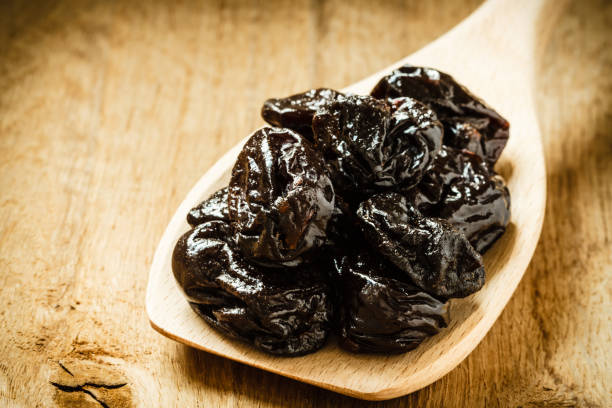 dried plums prunes on wooden spoon stock photo