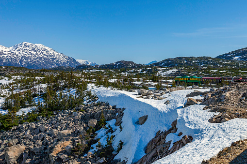 View of the White Pass Mountain Tourist Railway as it starts its journey from Skagway Alaska though the forests and white capped mountains ahead - eventually reaching the Canadian boarder
