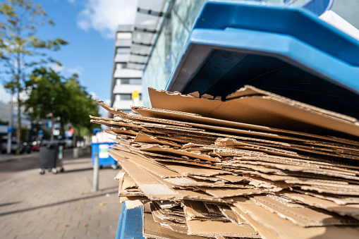 Used flattened cardboard boxes waiting to be collected in a blue plastic container for paper waste separation and recycling.