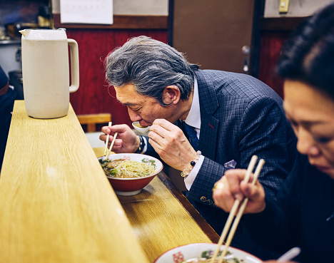 A group of customers enjoying traditional ramen noodles in a small ramen shop in Tokyo, Japan.