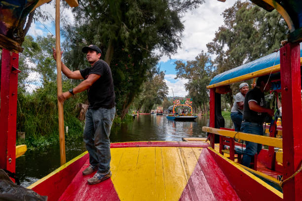 Traditional trajinero rowing a boat in Xochimilco Xochimilco, Mexico City, June 25, 2019 - The trajinero traditional rower of Xochimilco's trajineras, we see him while rowing his trajinera in channel combined with the other trajineras. trajinera stock pictures, royalty-free photos & images