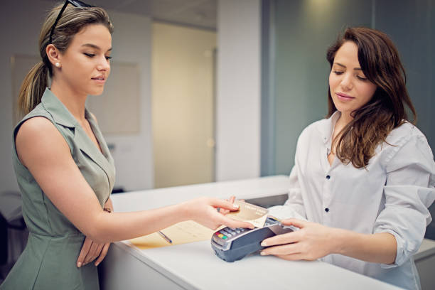 frau zahlt an der rezeption in schönheitsbehandlungsklinik mit kontaktloser kreditkarte - healthcare and medicine receptionist paying credit card stock-fotos und bilder