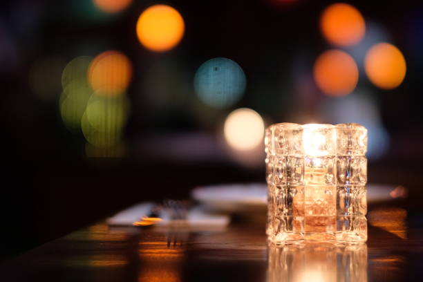 close up candle light in glass on table. Colorful defocused illuminations, plate and fork. Black background. Bar and restaurant concept candle light dinner stock pictures, royalty-free photos & images