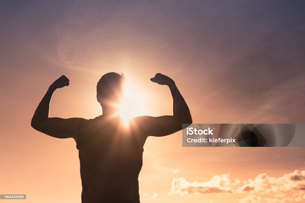 Strong man at sunset Strong winning man flexing arms facing sunset. Strength Stock Photo