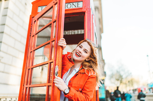 Portrait of a young woman in red, standing in front of the red phone box in London