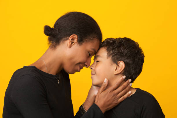 Studio portrait of mixed race mother with son on yellow background Studio portrait of mixed race mother with son on yellow background childrens day photos stock pictures, royalty-free photos & images