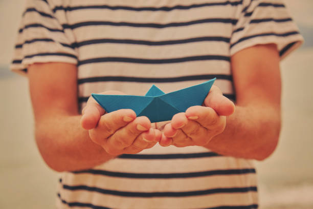 istock Man holding paper boat on tropical beach. 1164227793