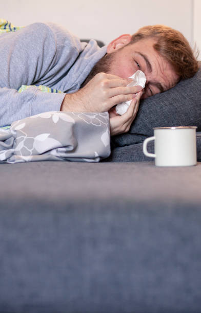 istock one young man, feeling sick, wiping his nose while laying in bed 1164230602