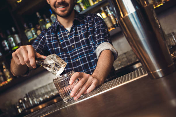 istock Young bartender standing at bar counter putting ice cube into glass joyful 1164234052