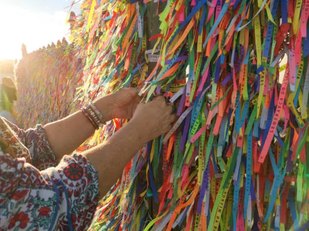 Photo of Hands tying Colorful ribbons on grid in front of Bonfim Church in Salvador, Bahia, Brazil