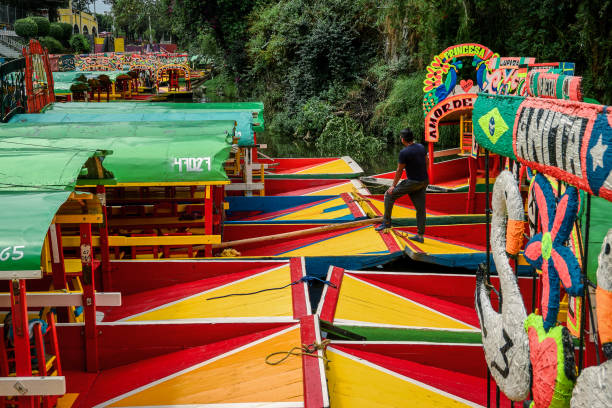 Man on trajinera moored in embarcadero of Xochimilco Xochimilco, Mexico City, June 25, 2019 -Man standing on trajinera moored in Embarcadero Nativitas trajinera stock pictures, royalty-free photos & images