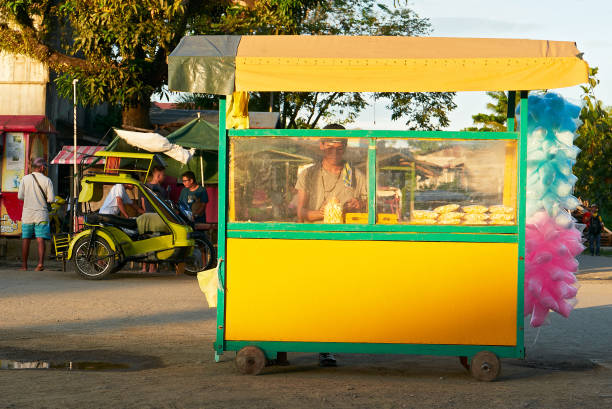 Man selling popcorn and colorful cotton candy in a cart Cuartero, Capiz Province, Philippines - June 7, 2019: Young man selling popcorn and colorful cotton candy in a small yellow push cart late afternoon philippines tricycle stock pictures, royalty-free photos & images