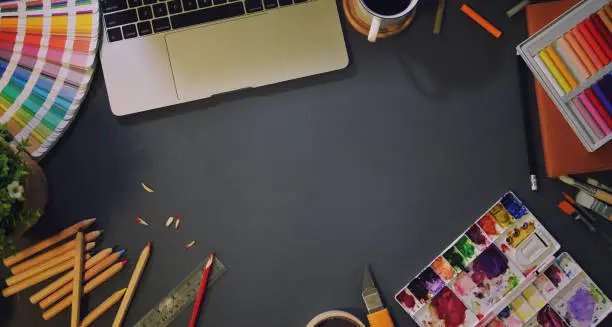 Top view of artist creative studio with paintings tools, stationery and laptop in dark background