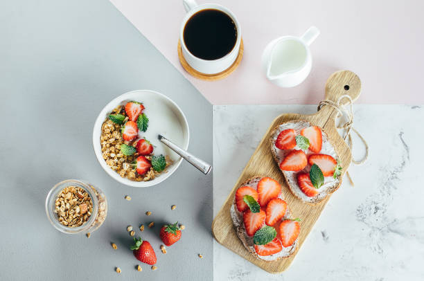 concepto de desayuno saludable. tostadas con queso cottage y fresa, yogur con granola y taza de café sobre fondo elegante tricolor, vista superior, plana. salud, pérdida de peso, concepto de alimentos dietéticos - yogurt yogurt container strawberry spoon fotografías e imágenes de stock