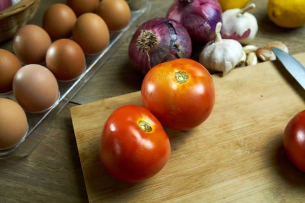 A plate of fresh cherry tomatoes sits on a wooden table, glistening with moisture under natural light. Green lettuce and avocado are slightly blurred in the foreground, adding a fresh and organic feel.