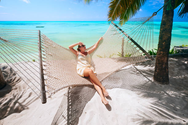 Woman is relaxing in a hammock on the beach among the palm near the sea. stock photo