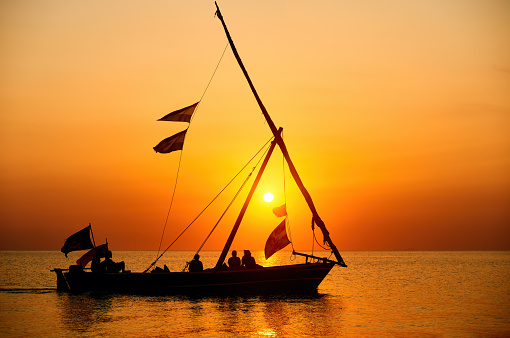 Tourists sail in a traditional boat and enjoy the colorful sunset on the island of Zanzibar, Tanzania. Happy friends enjoy summer vacation.