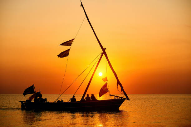 Tourists sail in a traditional boat and enjoy the colorful sunset on the island of Zanzibar,Tanzania. stock photo