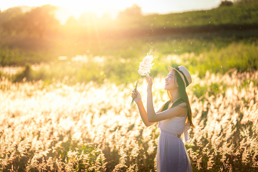 Beauty Asian Girl Outdoors enjoying nature. Beautiful Teenage Model girl in white dress running on the Spring Field, Sun Light.
