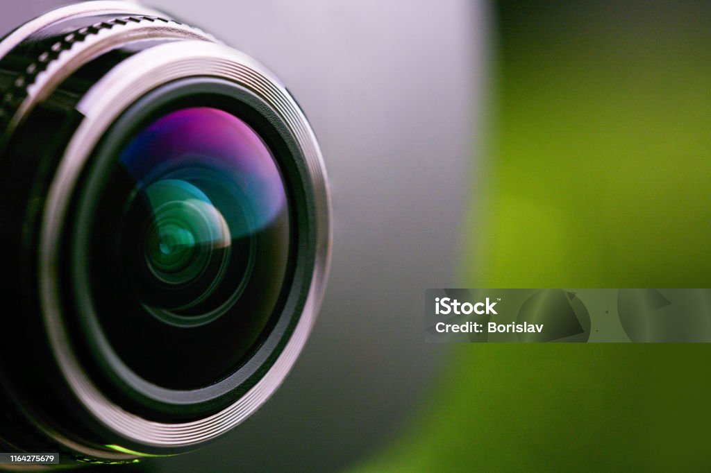 Camera lens with green backlight. Side view of the lens of camera on green background. Greencamera Lens close Up. Pure red Home Video Camera Stock Photo