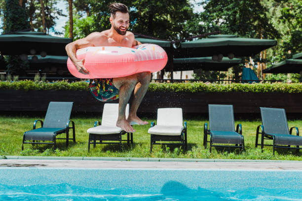 istock happy bearded man with barefoot jumping in water while holding inflatable ring 1164283802