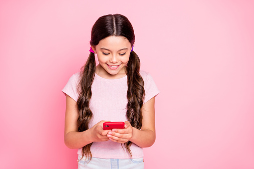 Portrait of charming kid holding, device looking searching news wearing white t-shirt isolated over pink background