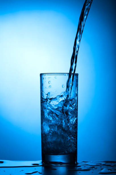istock Water pours into a glass on a blue background 1164288612