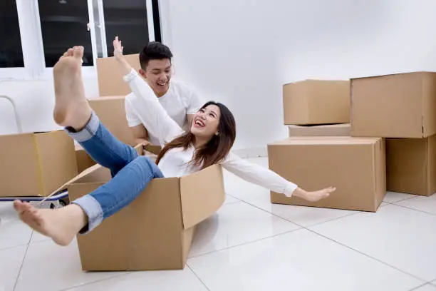 Picture of happy Asian couple playing with a cardboard box while moving into a new house