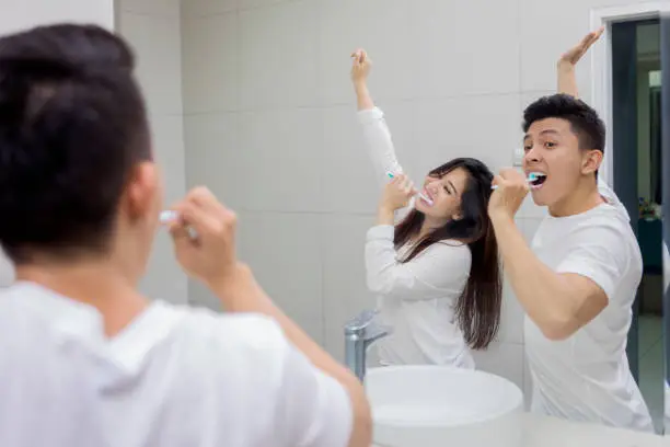 Portrait of happy young couple brushing teeth in the bathroom while dancing front a mirror