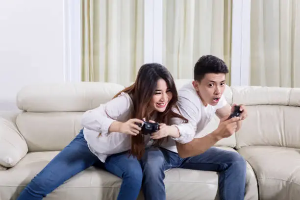 Picture of happy couple playing video games while sitting on the sofa. Shot at home